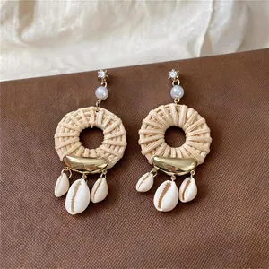 Close-up of bohemian woven straw earrings with natural cowrie shell and pearl details