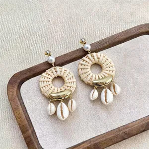 Detail showing bohemian woven rattan hoop earrings with natural shell pendants.