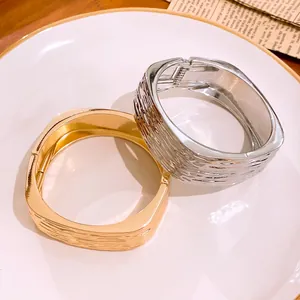 Detailansicht der exquisiten Faltenstruktur quadratischer Armreifen in Gold und Silber.