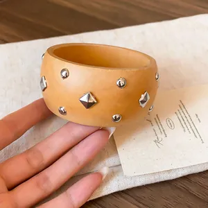 Detalle de brazalete marrón claro con remaches plateados redondos y en forma de rombo