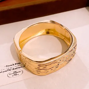Detailansicht der Rippeltextur auf einem quadratischen goldfarbenen Mode-Armreif.