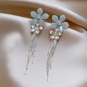 Détail de boucles d'oreilles fleur bleue avec zircon et longues franges argentées