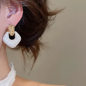 Dichtbij van elegante goudkleurige oorknopjes met witte marmeren vierkante hars hanger decor