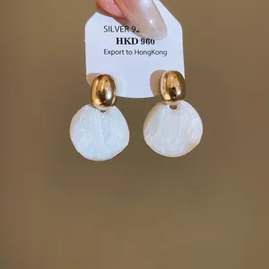 Detail van elegante goud- en witkleurige ronde druppeloorbellen met zilveren naalden.