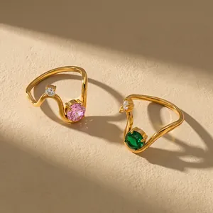 Close-up of gold geometric wave rings with pink and green zircon stones in natural sunlight