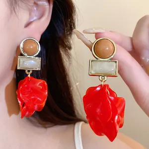 Detailed view of exaggerated red acrylic petal earrings with brown and white bead accents