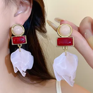 Close-up detail of geometric acrylic earrings with red stone and white flower petals