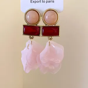 Detail view of gold-tone earrings with red rectangular and pink petal acrylic charms