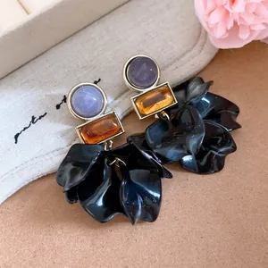 Detail view of oversized acrylic petal earrings with purple and amber stone accents.