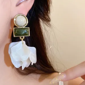 Detailed macro view of white acrylic petal earrings featuring green stone accents