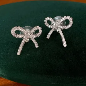 Boucles d'oreilles clips nœud argentées ornées de zirconiums sur un velours vert.