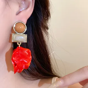 Close-up of large red acrylic petal drop earrings with geometric studs.