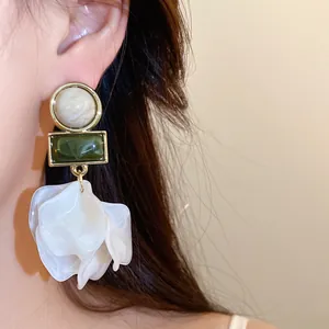 Detail shot of large white acrylic petal earrings with green geometric stones.