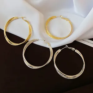 Nahaufnahme von eleganten gold- und silberfarbenen mehrlagigen Creolen auf weißer Seide
