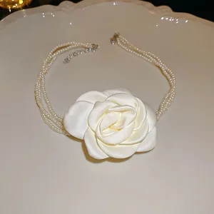 Nahaufnahme einer eleganten weißen Stoffblume und einer mehrlagigen Perlenkette auf einem Teller.