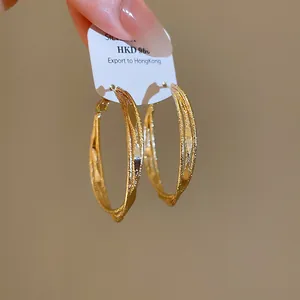 Detailansicht goldfarbener, dreilagiger, gedrehter Creolen mit strukturierter Oberfläche