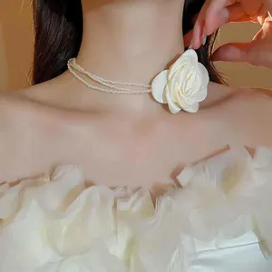 Nahaufnahme von eleganten weißen Stoffblumen und mehrlagiger Perlen-Choker-Halskette