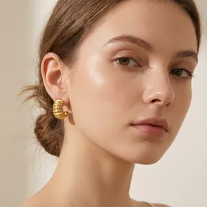 Close-up view of gold plated stainless steel pleated hoop earrings on a model's ear