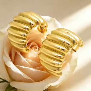 Macro view of gold-plated pleated stainless steel hoop earrings resting on a rose petal