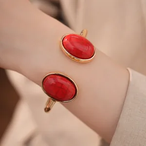 Detailansicht eines goldenen Manschettenarmbands mit zwei großen roten Steinen am Handgelenk.