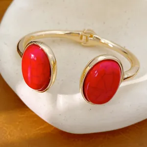 Detailansicht eines eleganten goldenen Armreifs mit zwei großen ovalen roten Steinen.