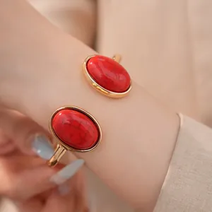Detailansicht eines luxuriösen goldenen Armreifs mit zwei großen roten ovalen Steinen.