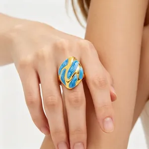 Detalle de anillo abstracto de esmalte azul y acero de titanio dorado en el dedo.