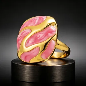 Vista macro de un anillo esmaltado rosa jaspeado con baño de oro y diseño ondulado.