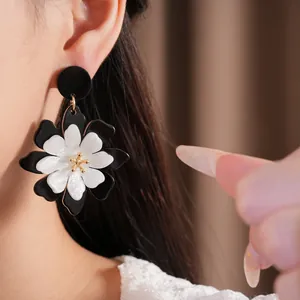 Close-up detail of oversized black and white acrylic flower earrings with gold center.