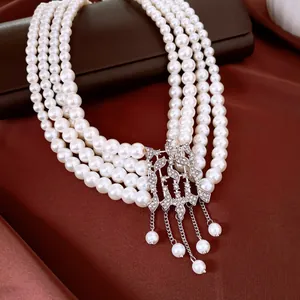 Détail du collier de perles à quatre rangs avec fermoir géométrique en strass et pompons.