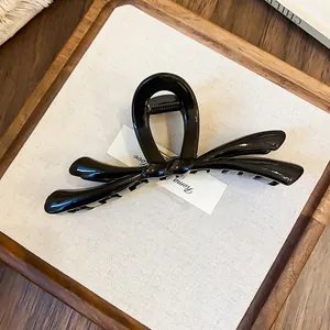 Vista detallada de una elegante pinza para el pelo con lazo negro en una bandeja de madera