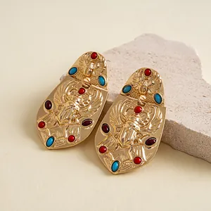Primer plano de pendientes de escarabajo vintage dorados con gemas de acrílico sobre una piedra