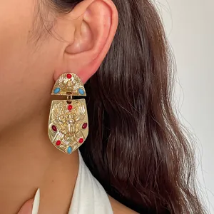 Vista detallada de pendientes vintage dorados con motivo de escarabajo egipcio y piedras.