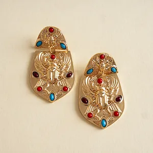 Detalle de pendientes escarabajo egipcio vintage en oro con piedras de colores sobre crema