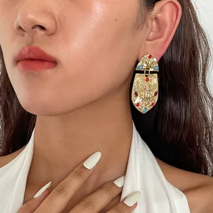 Primer plano de modelo con pendientes vintage dorados en forma de escudo y cristales
