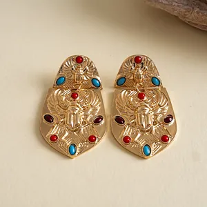 Primer plano de pendientes de escarabajo vintage dorados con piedras rojas y azules