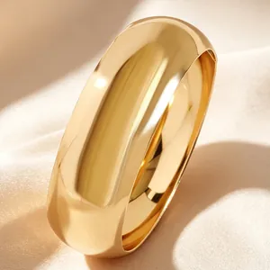 Vista detallada de un brazalete dorado ancho con acabado de espejo sobre fondo seda