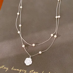 Detalle elegante de un collar de plata de dos capas con perlas y un colgante de flor de circón