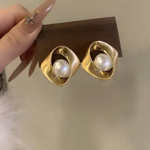 Gros plan de boucles d'oreilles dorées torsadées avec une perle blanche élégante.
