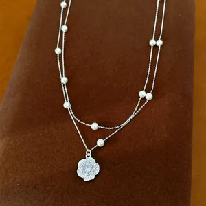 Vista detallada de un collar de dos capas con perlas y un colgante de flor brillante