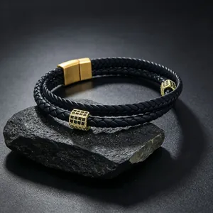 Détail d'un bracelet en cuir tressé double couche avec des breloques en zircone plaquées or.