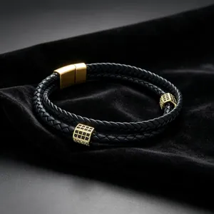 Détail d'un bracelet en cuir tressé noir double couche avec des breloques dorées en zircone.