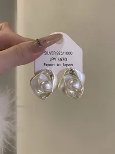 Détail de boucles d'oreilles argentées torsadées avec une perle blanche