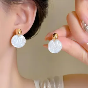 Gros plan de boucles d'oreilles rondes nacrées blanches avec clous dorés pour un look luxe
