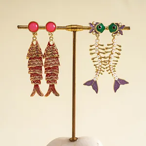 Vue détaillée de boucles d'oreilles créatives en forme de carpe et squelette perlé.