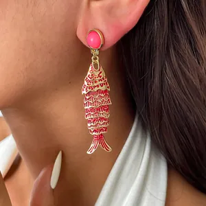 Détail d'une boucle d'oreille pendante poisson en émail rouge portée par un mannequin.