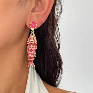 Gros plan d'une boucle d'oreille créative en émail rouge en forme de poisson sur l'oreille