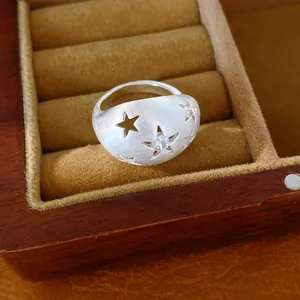 Close-up van een geborstelde zilveren ovale ring met zirkonia en sterren in een doosje.