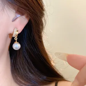Close-up of elegant gold hoop earring with sparkling zircons and a white pearl drop
