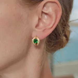 Close-up of a gold-toned earring featuring a square emerald green zircon and white accents